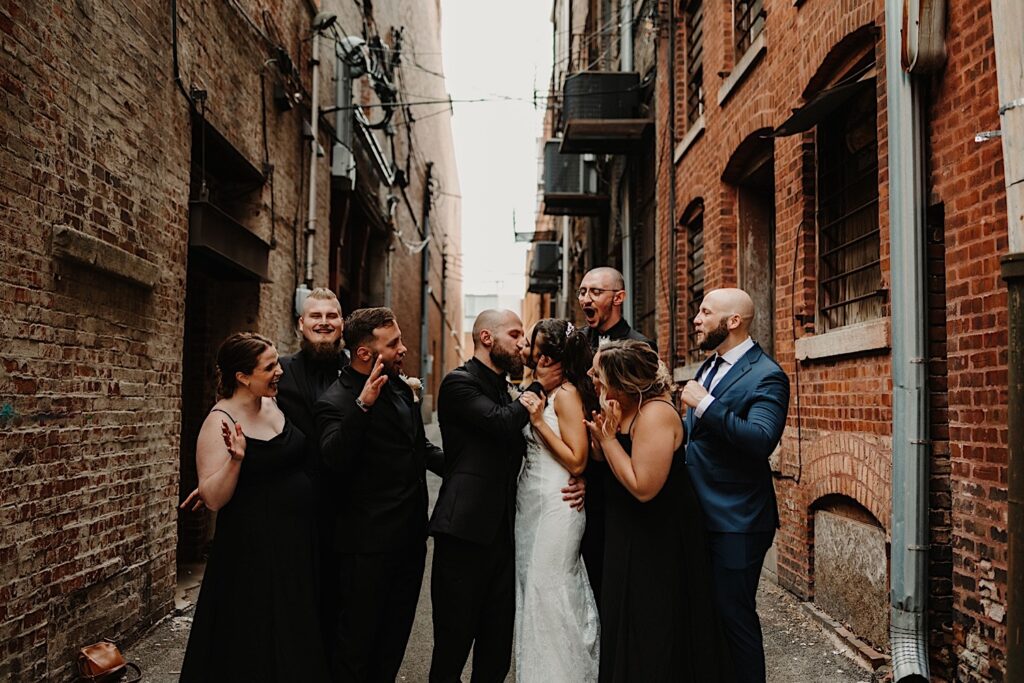 A bride and groom kiss in an alley outside of Reality on Monroe while their wedding parties crowd around them and cheer
