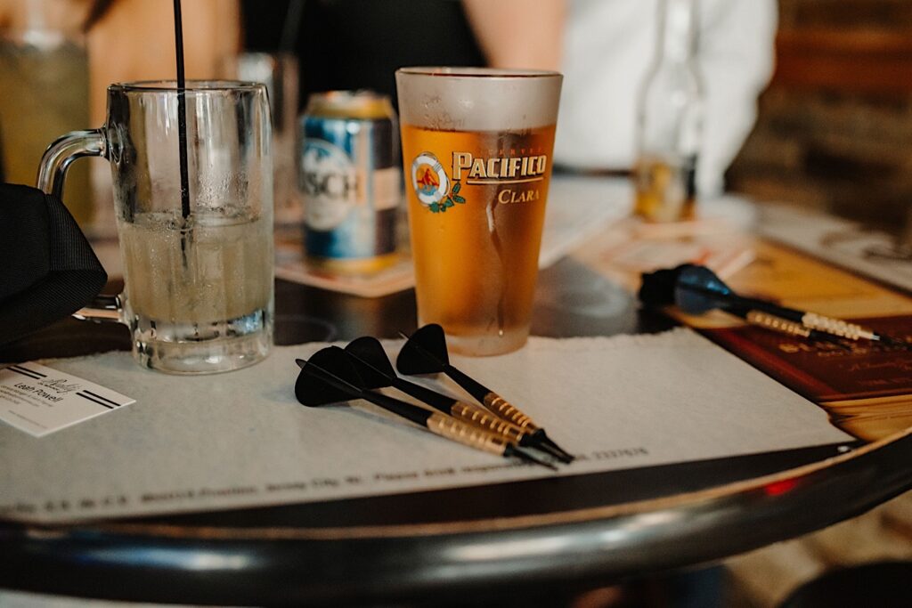 Detail photo of darts on a table next to a Pacifico beer glass and a drink in a pitcher