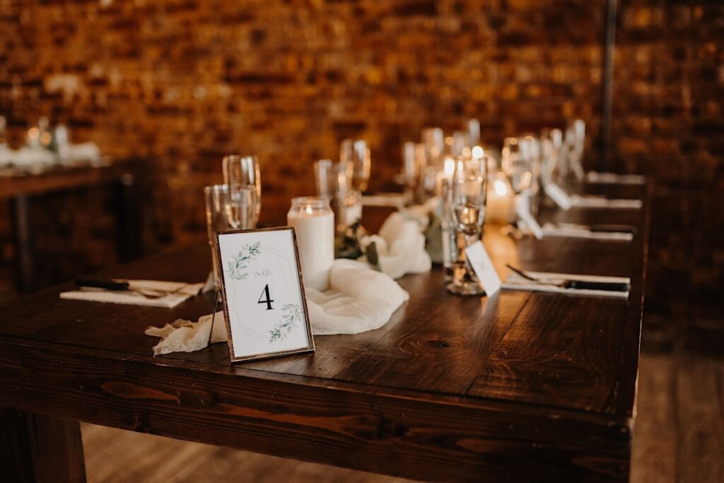 A wooden table with a picture frame on it reading "Table 4" is decorated for a wedding reception with candles and white fabric