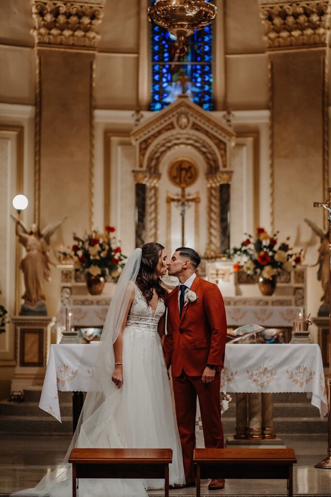 During their wedding ceremony in a church a bride and groom stand side by side and kiss one another