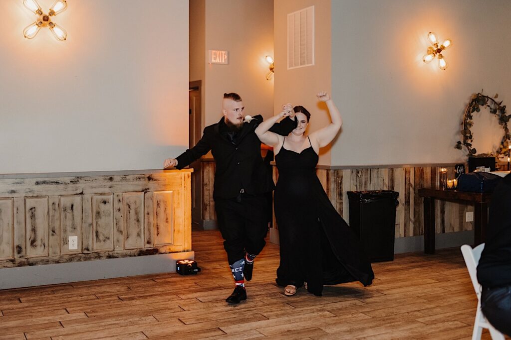 A bridesmaid and a groomsman enter a wedding reception and lift their aarms in the air