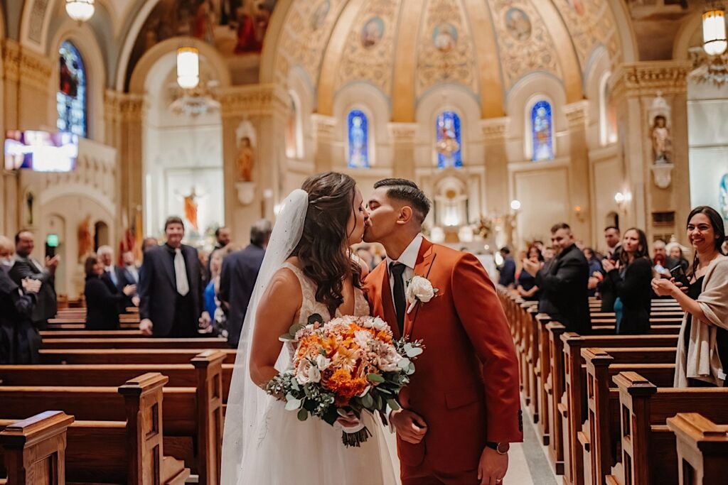 A bride and groom kiss one another in a church after walking down the aisle following their wedding ceremony