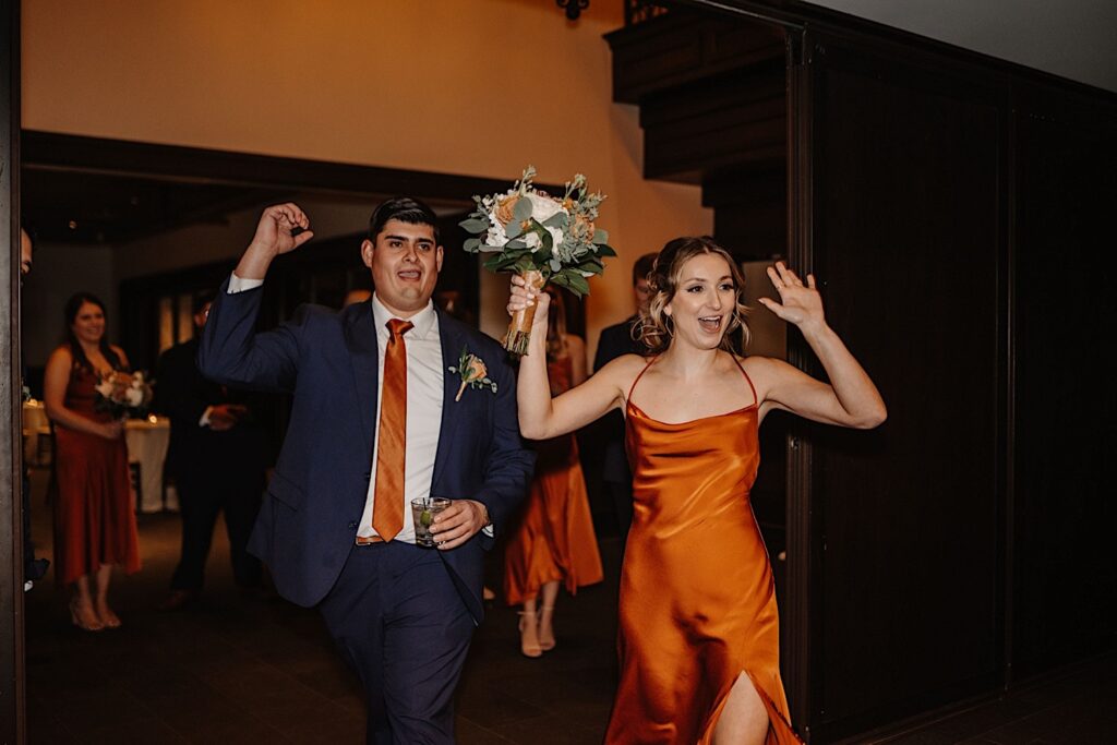 A bridesmaid and groomsman enter a fall wedding reception at Mistwood Golf Club and celebrate to hype the crowd up before the bride and groom enter