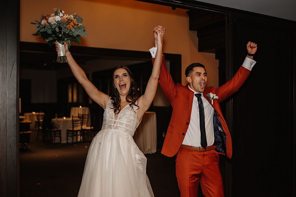 A bride and groom exclaim and lift their arms in the air while entering their fall wedding reception at Mistwood Golf Club