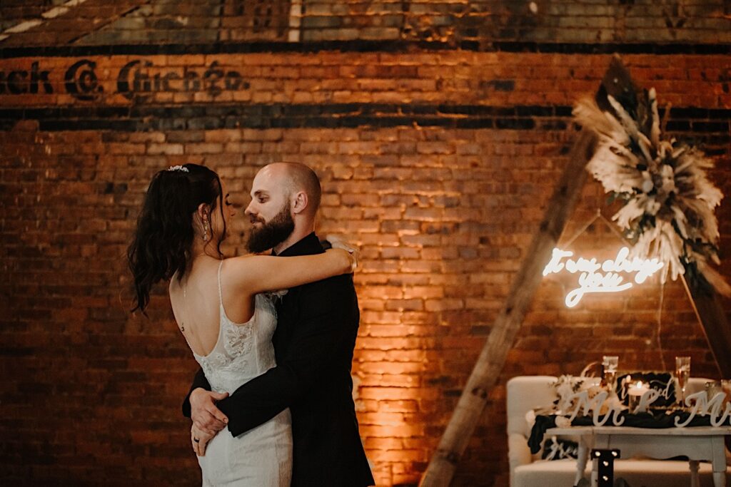 A bride and groom look at one another while dancing in front of a brick wall in their wedding venue Reality on Monroe
