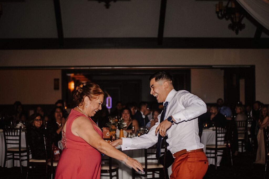 A groom and his mother smile as guests watch them dance during their fall wedding reception at Mistwood Golf Club