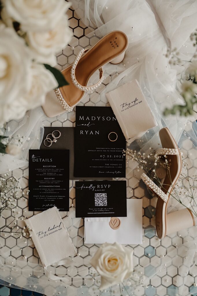 A wedding day flat lay consisting of invites, RSVP's shoes, flowers, rings and fabric