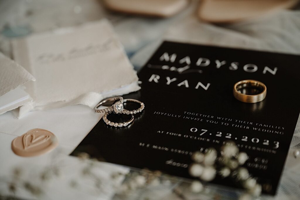 Detail photo of wedding and engagement rings laying on a wedding invite on a table