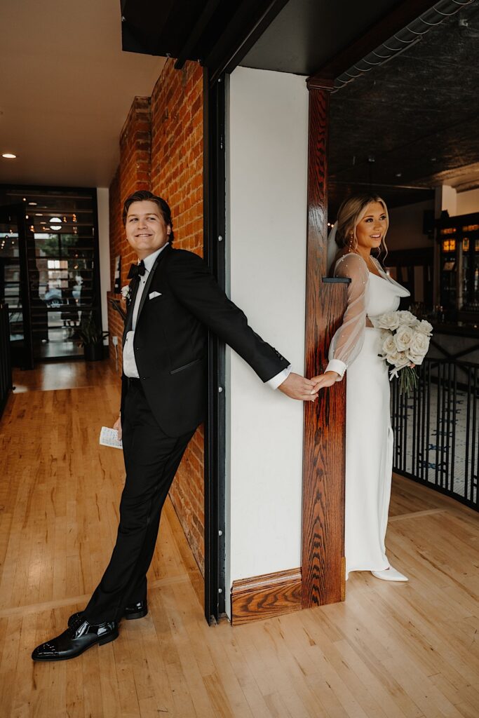 A bride and groom stand on opposite sides of a wall and hold hands in a doorway in what's called a first touch, so they wouldn't see one another prior to their wedding day