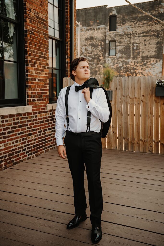 Portrait photo of a groom with his suit coat over his shoulder while standing on an outdoor back patio