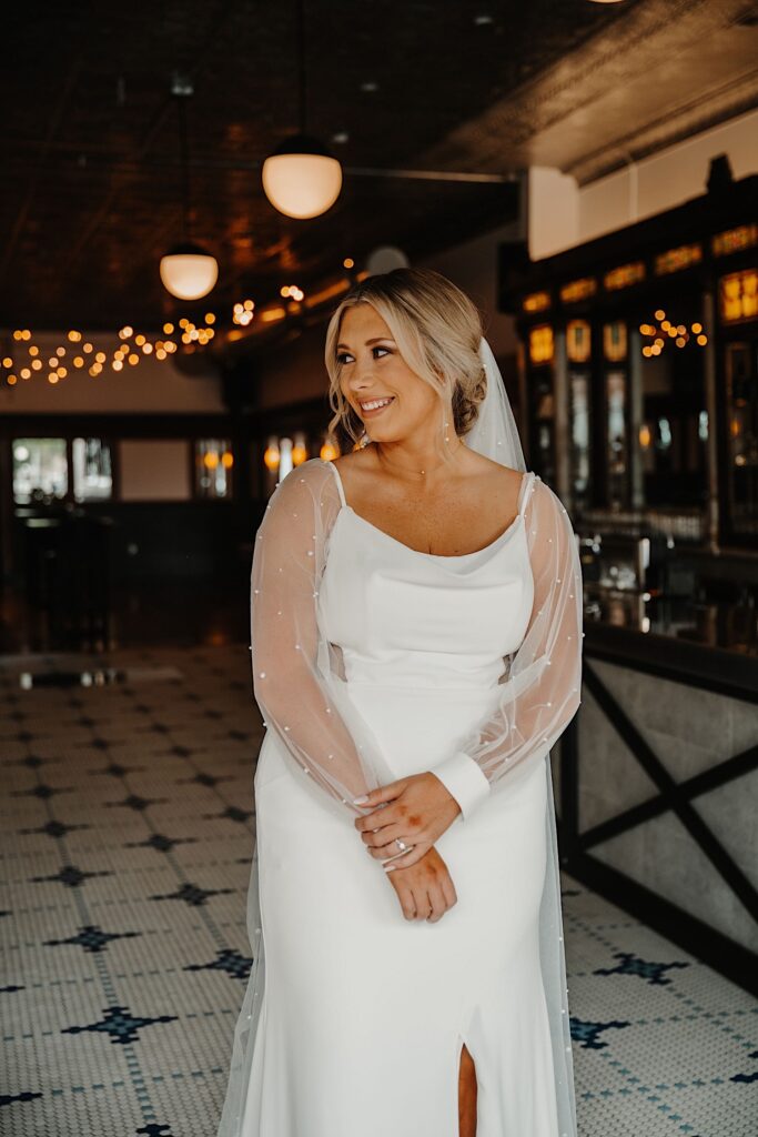 Portrait photo of a bride in her wedding dress standing in side of her wedding venue and smiling to the left