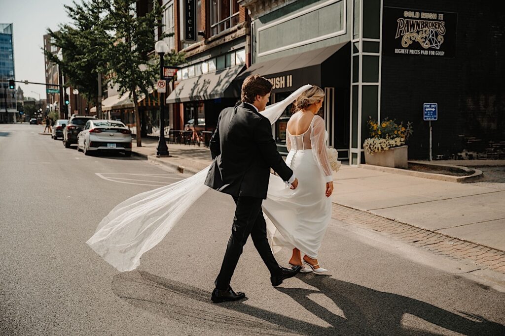 A bride and groom walk across a street in Champaign Illinois together after their wedding ceremony at Venue CU