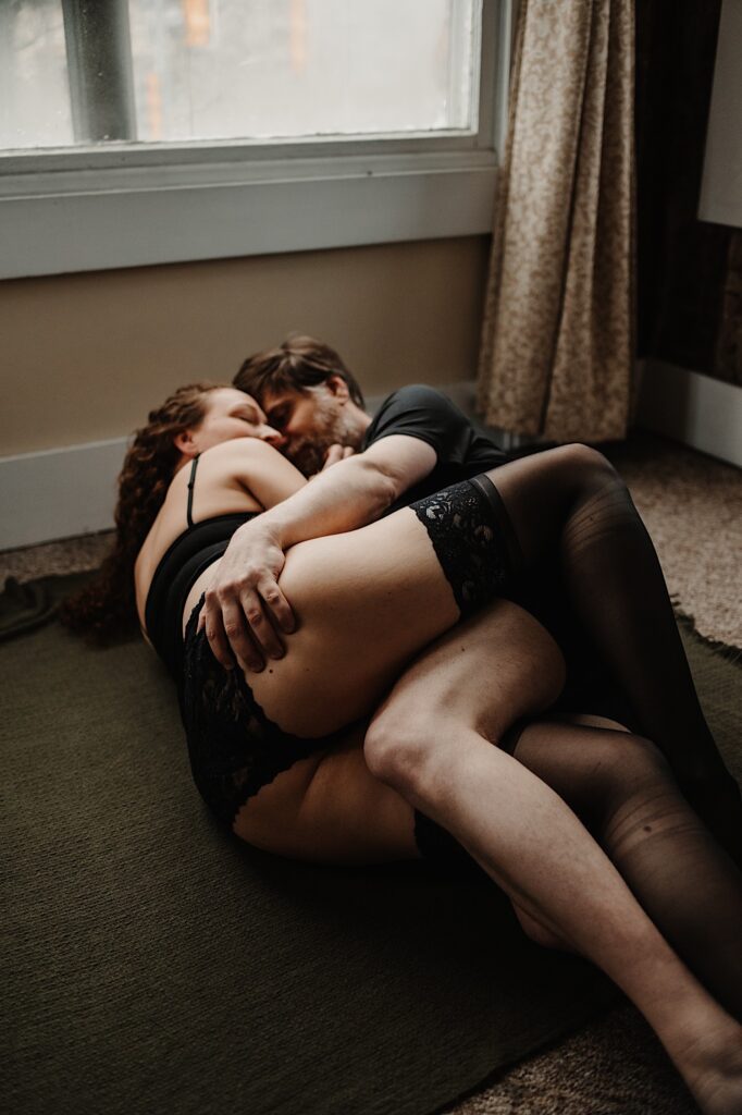 A man and woman lay on the floor with one another, the woman is in lingerie and the man is grabbing her behind
