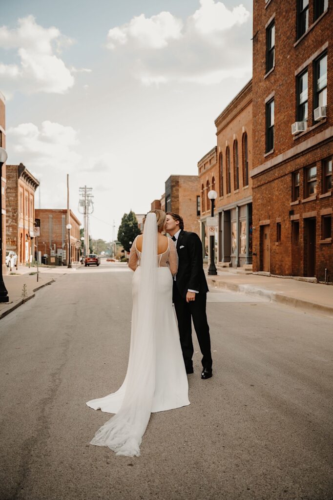A bride and groom kiss one another with the bride facing away from the camera while they stand on a street in Champaign Illinois