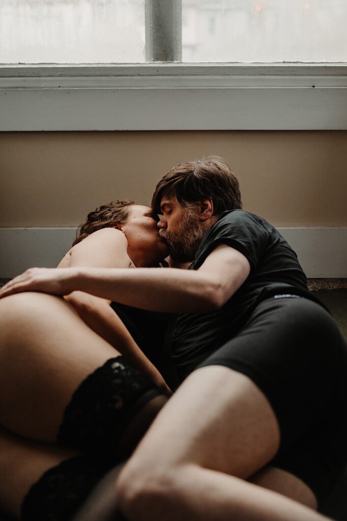 A man and woman lay on the floor with one another and kiss