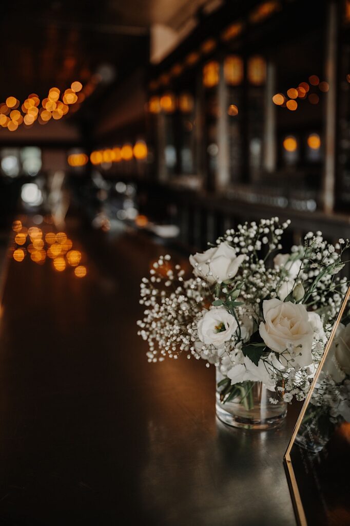 Detail photo of a small glass with white flowers in it sitting on a bar top