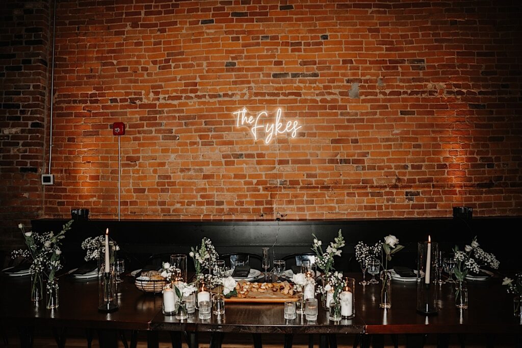 A brick wall inside the wedding venue, Venue CU in Champaign has a neon sign on it that reads "The Fykes" hangs above the head table