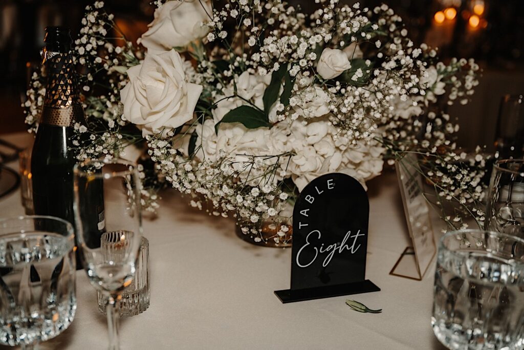A table set up for a wedding reception with glassware, champagne, a table sign that reads "table 8", flowers, and more