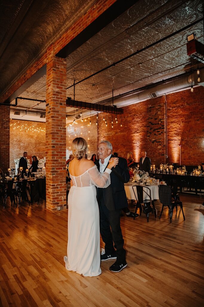 A bride and her grandfather dance together during her wedding reception at Venue CU as guests watch