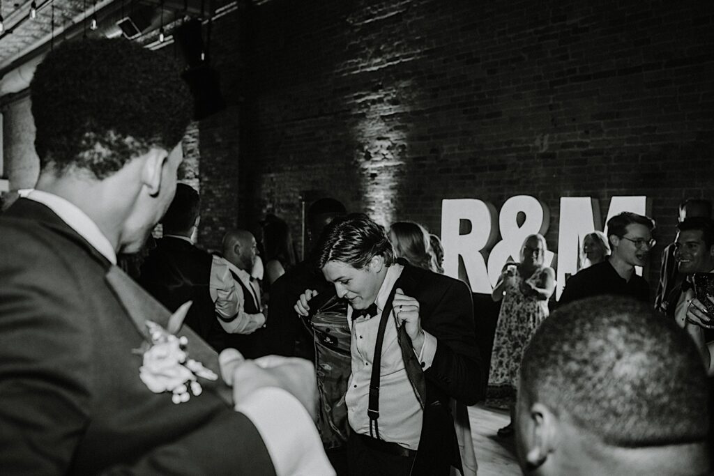 Black and white photo of a groom dancing with guests of his wedding during his indoor reception at Venue CU in Champaign Illinois 