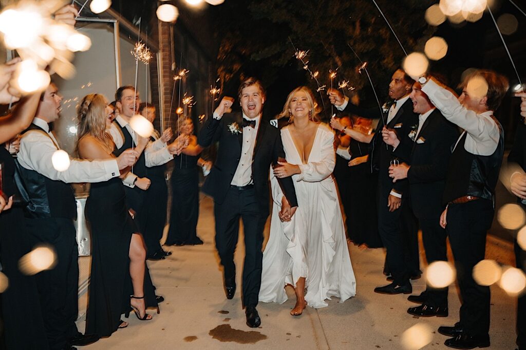 A bride and groom walk together and smile while their guests around them form a tunnel with sparklers as they exit their wedding at Venue CU in Champaign Illinois