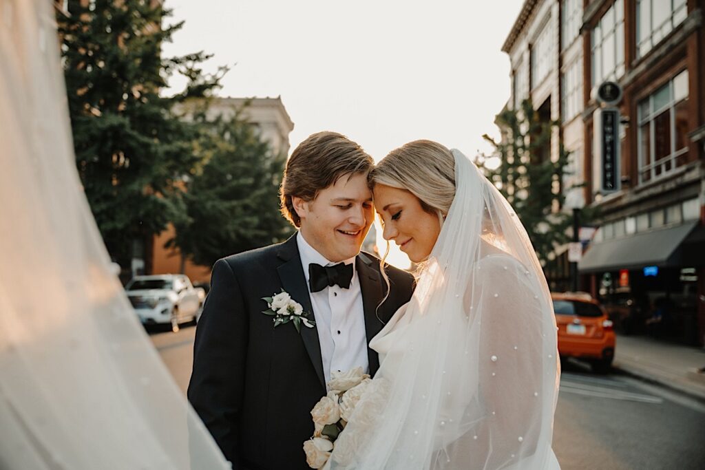 A bride and groom stand in a street in Champaign Illinois during sunset and pose with one another while smiling outside their wedding venue, Venue CU