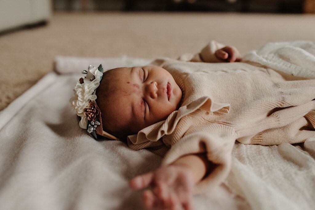 Photo of a sleeping newborn baby laying on a blanket with a flower bow on their head during their in-home session