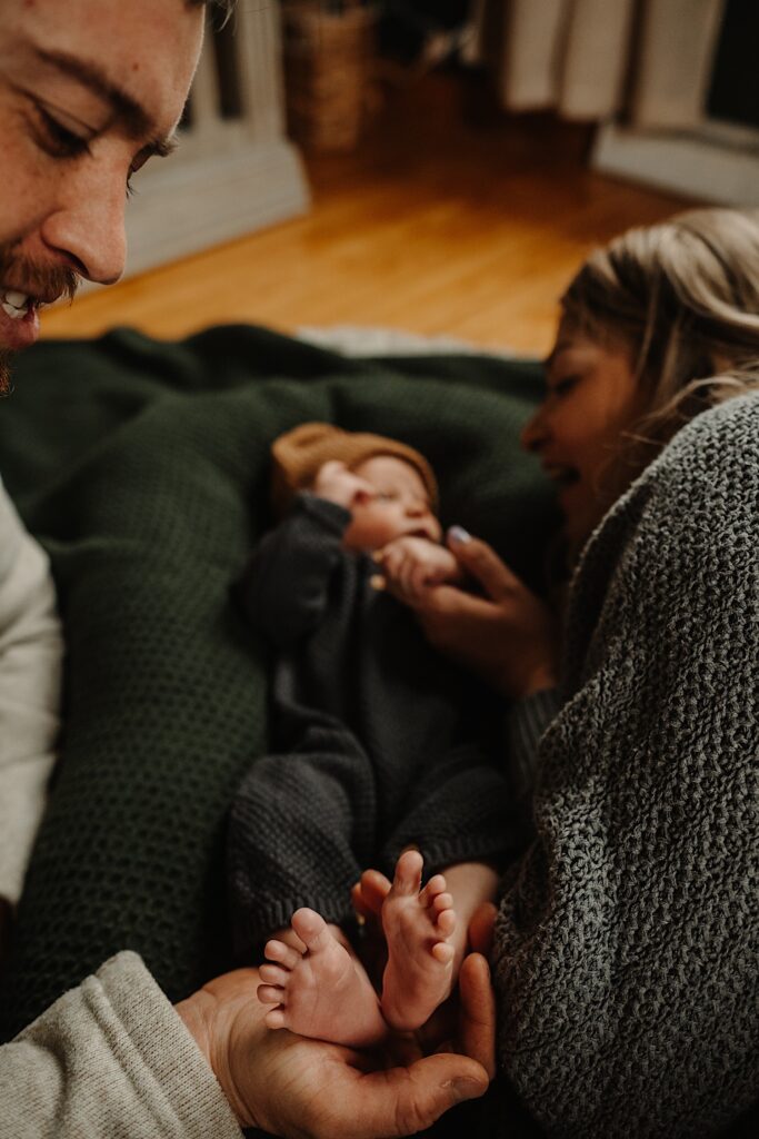 A mother talks to her newborn baby while the father smiles playing with the baby's feet