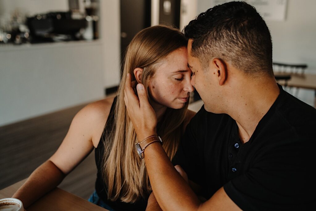 A woman closes her eyes while leaning her head against the head of a man sitting next to her during their engagement session in Bloomington, Illinois