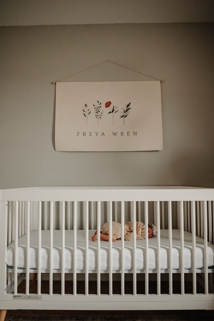 A newborn baby sleeps in her crib as a flag with her name on it hangs above the crib