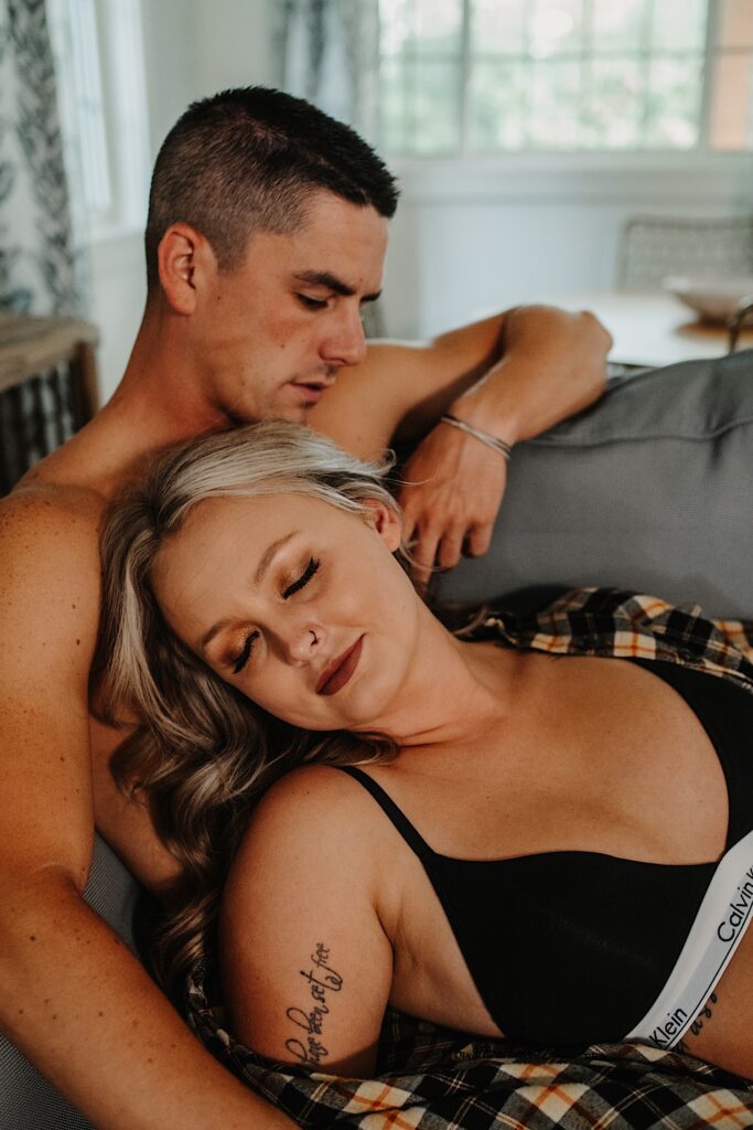 A woman in her underwear lays on a man who is sitting on a couch shirtless