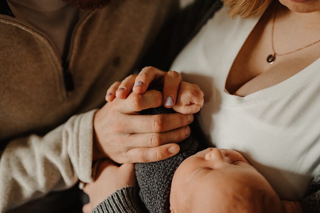 Close up photo of a mother and father holding the hand of their newborn infant for a photo during their in-home session