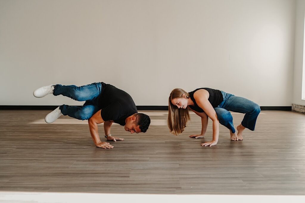 A man and woman perform yoga poses in a yoga studio together during their engagement session in Bloomington, Illinois