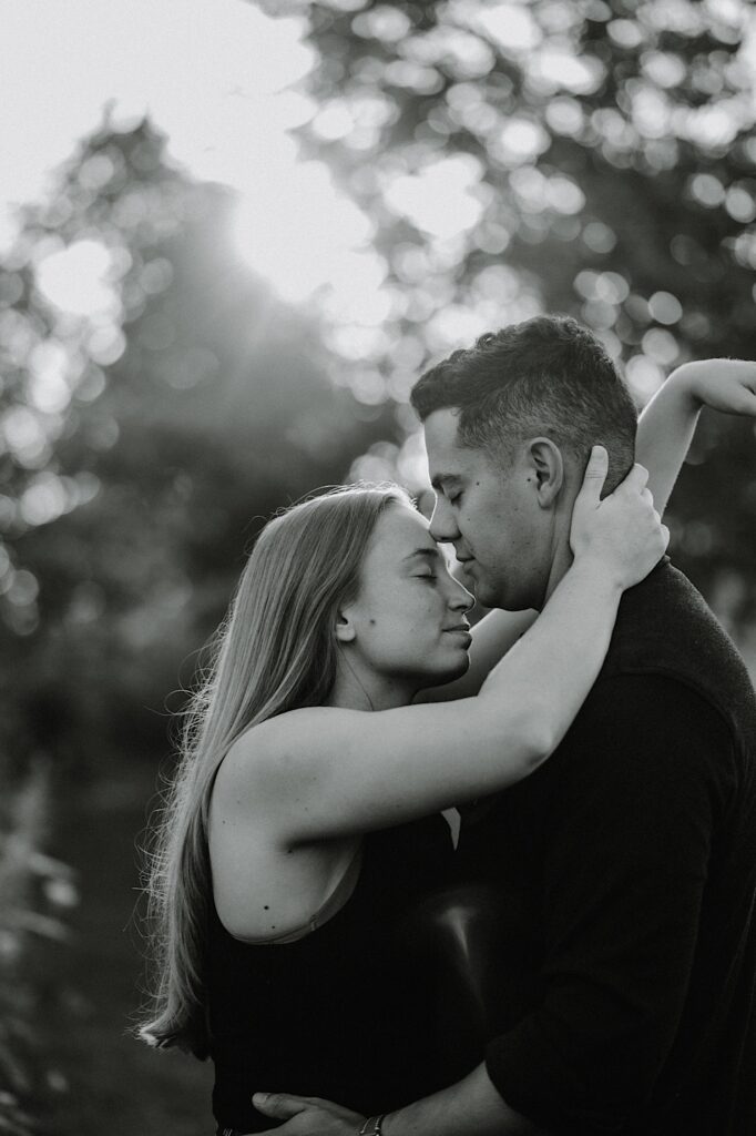 Black and white photo of a man and woman embracing with their eyes closed while in a park