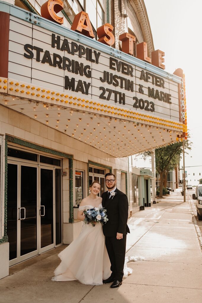 A bride and groom smile while standing next to one another as they stand outside of the Castle Theater