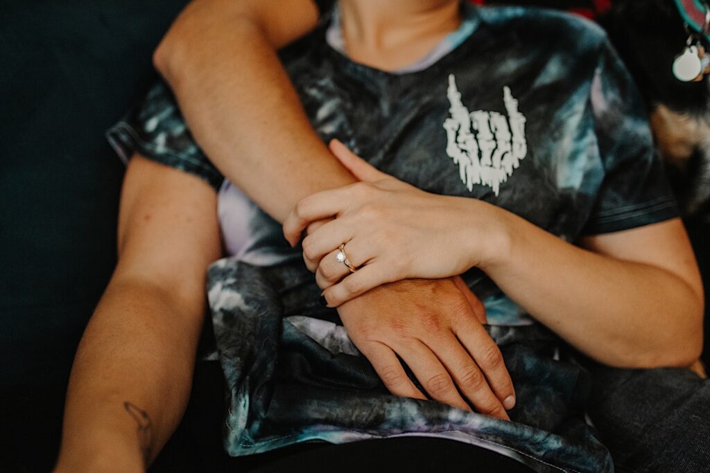 Close up photo of a woman wearing an engagement ring holding her partners arm that is wrapped around her