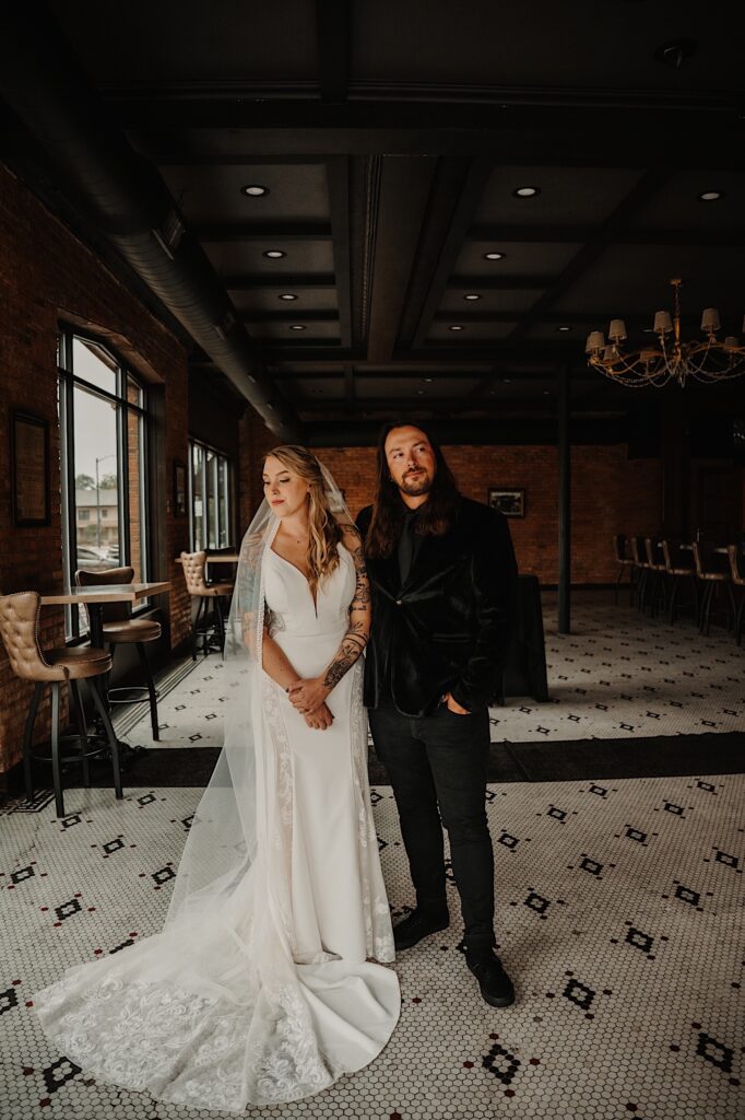 A bride and groom stand side by side for a portrait inside a brick building