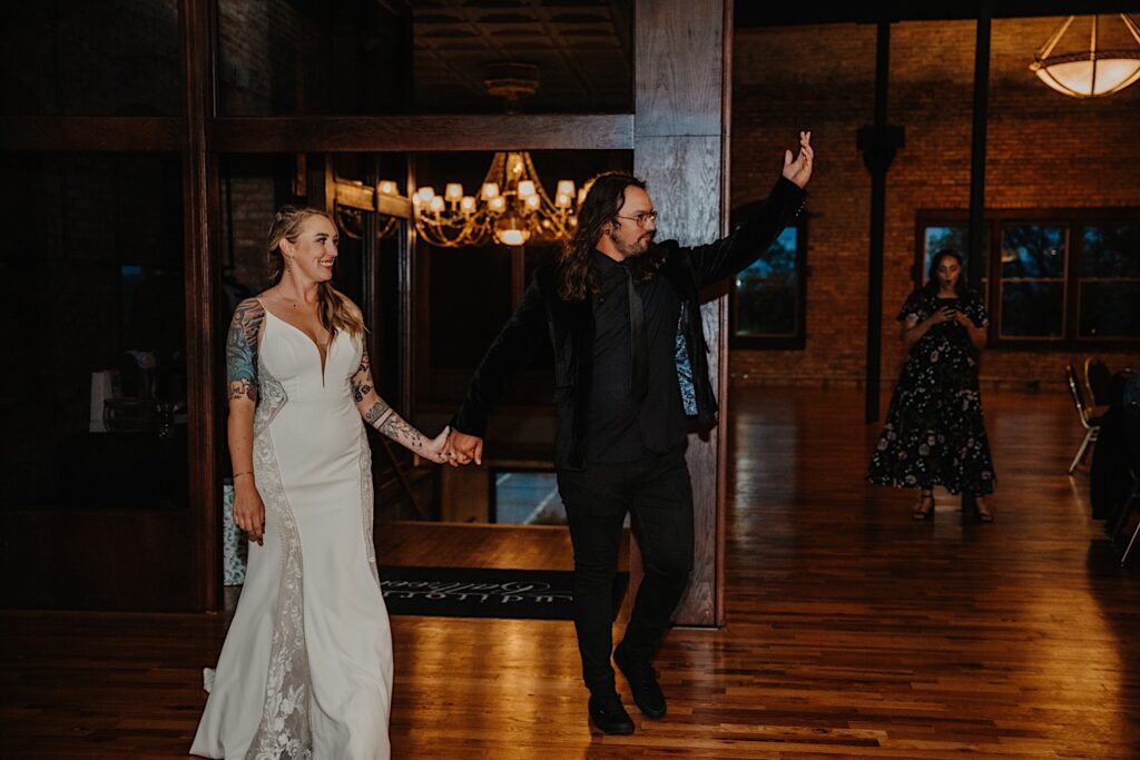 A bride and groom hold hands while entering their indoor wedding venue for the start of their reception