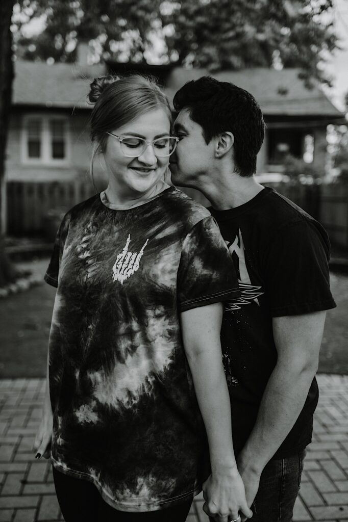 Black and white photo of a man whispering in a woman's ear as they stand outside in their backyard