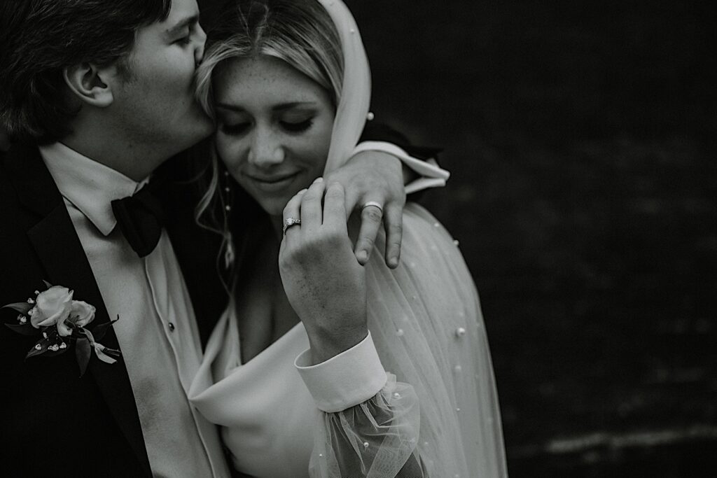 Black and white photo of a bride smiling with her eyes closed as the groom holds her hand and kisses her head, photo taken by a Central Illinois Wedding Photographer