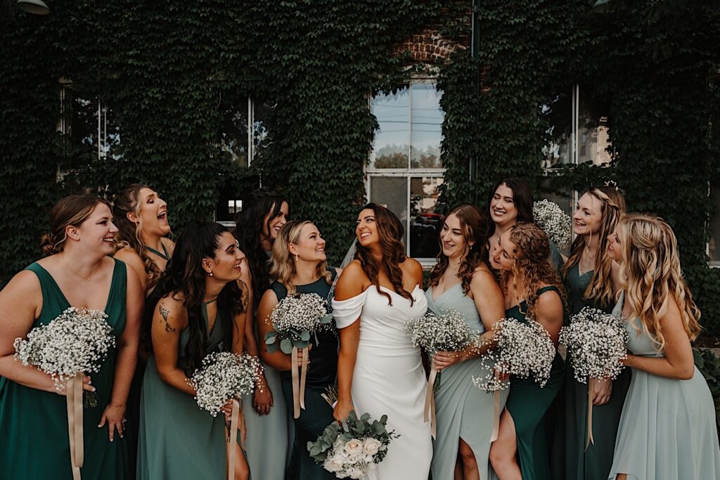 A bride smiles while surrounded by the 10 members of her wedding party while standing outside of the wedding venue, photo taken by a Central Illinois Wedding Photographer