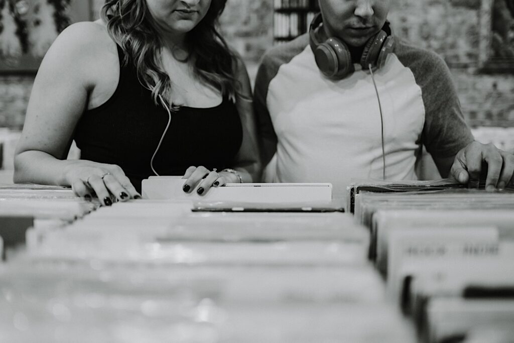Black and white photo of a couple looking through records together in a Chicago record store while they take engagement photos