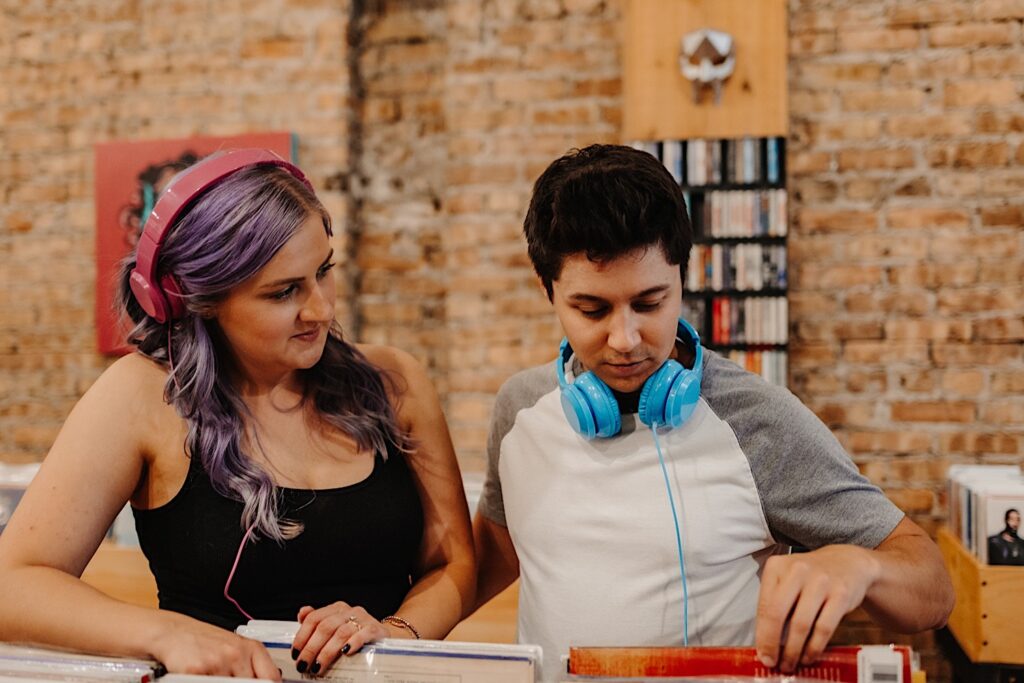 A man looks through records in a Chicago record store while a woman looks at him as they take their engagement photos