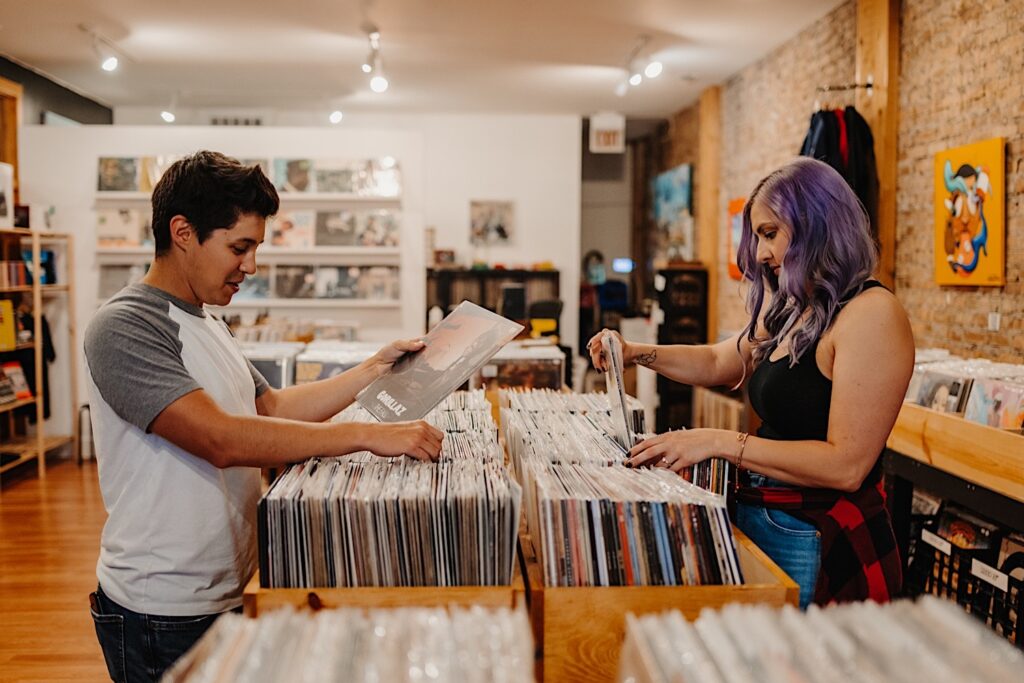 A couple stand across from one another while looking at records in a vinyl shop in Chicago during their engagement photos