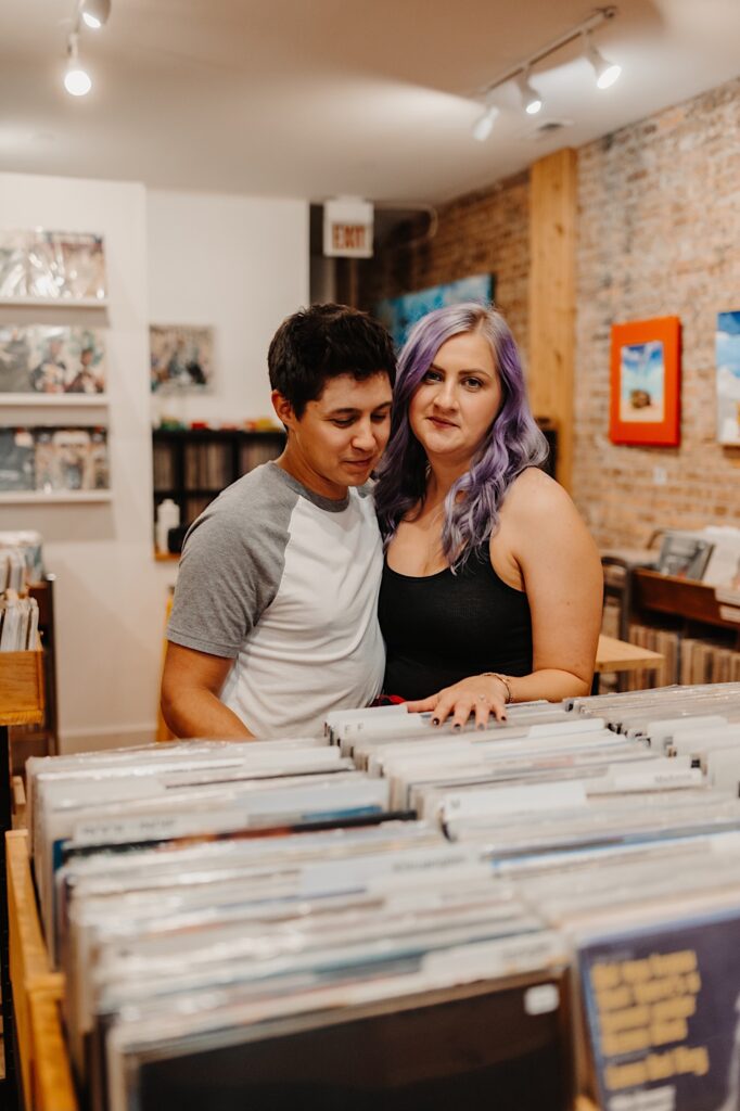 A woman looks at the camera while a man next to her looks at the vinyl in front of them while the two stand in a Chicago record store