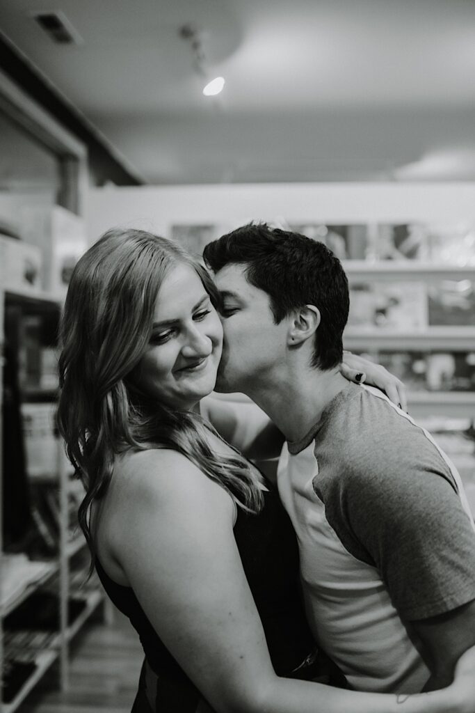 Black and white photo of a woman smiling while a man kisses her cheek while inside of a record store in Chicago
