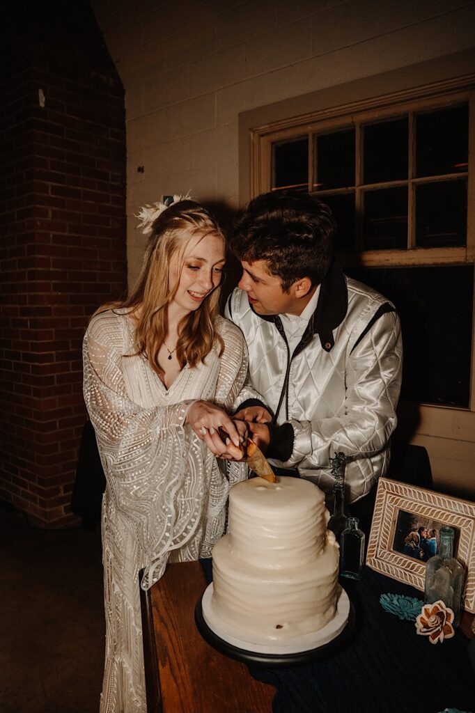 A bride and groom cut the cake together during their indoor wedding reception