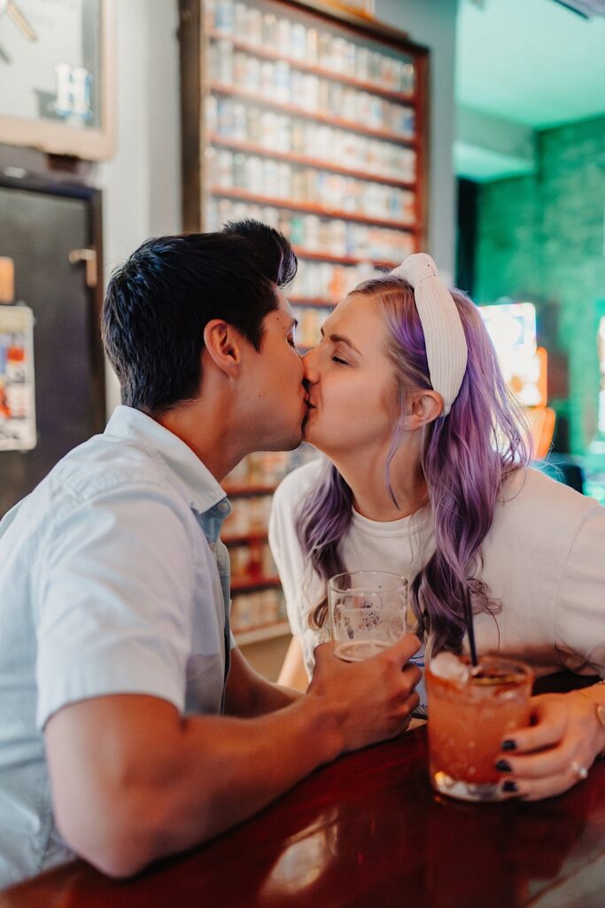 A couple kiss one another while holding their drinks as they sit at a bar in Chicago