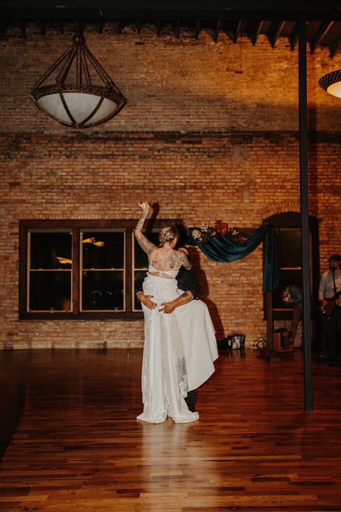 A bride lifts her arm in the air as the groom lifts her in the air during their indoor wedding reception