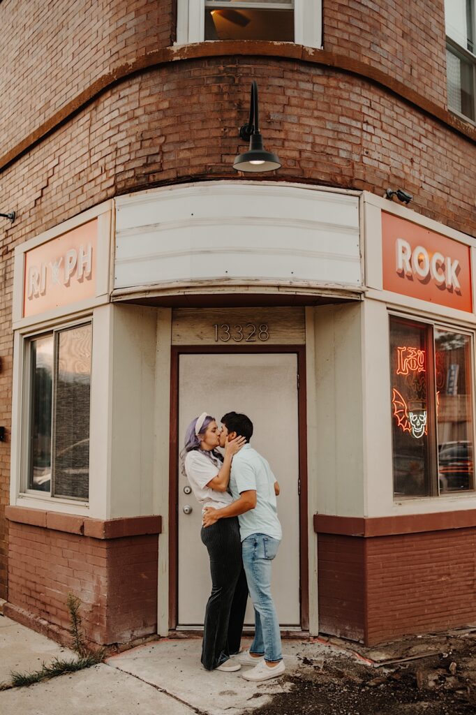 A couple kiss one another while standing outside the front door of a brick bar in Chicago